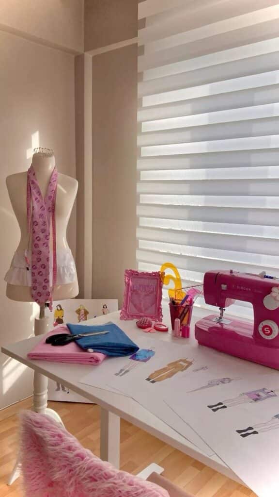 Fashion design workspace with mannequin, pink sewing machine, fabric, and sketches in sunlight.