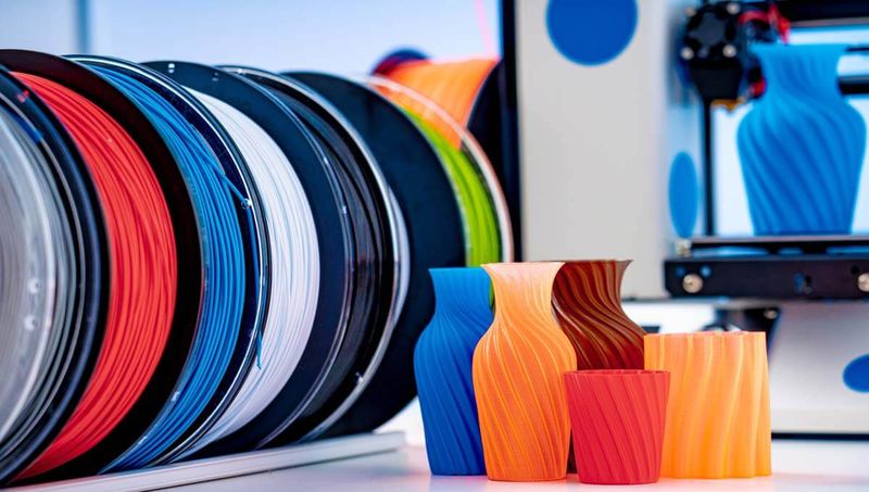 Colorful 3D printed objects and filament spools displayed near a 3D printer setup.