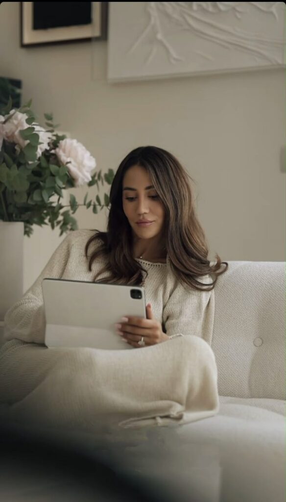 Woman relaxing on a sofa, using a tablet in a cozy, modern living room with flowers in the background.