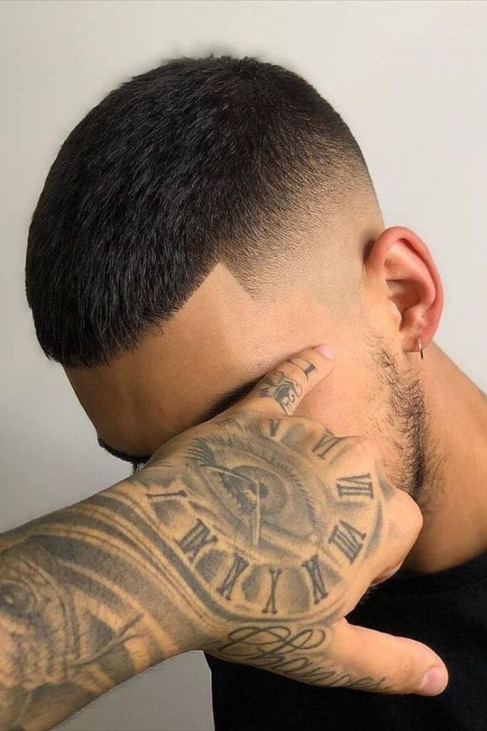 Close-up of a fresh fade haircut with tattooed hand in the foreground, showcasing intricate watch tattoo design.