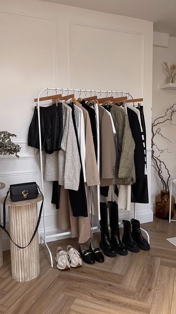 Clothing rack with neutral-toned outfits, boots, and accessories in a modern room with wood flooring and decor.