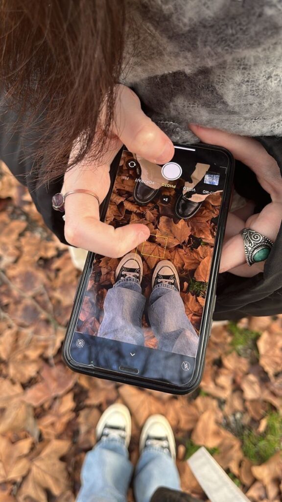 Close-up of a person taking a photo of shoes on autumn leaves with a smartphone.