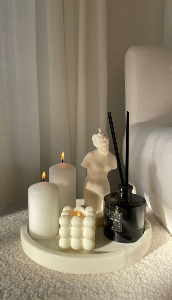 Minimalist decor with candles, statue candle, and reed diffuser on a round tray, creating a cozy ambiance.