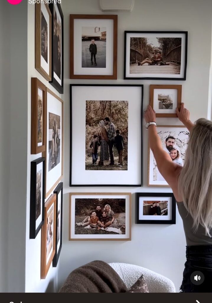 c9635fb7-661d-4fea-863c-1582ea7d0f18 Woman arranging family photo gallery wall with nature-themed decor. | Sky Rye Design Woman arranging family photo gallery wall with nature-themed decor.