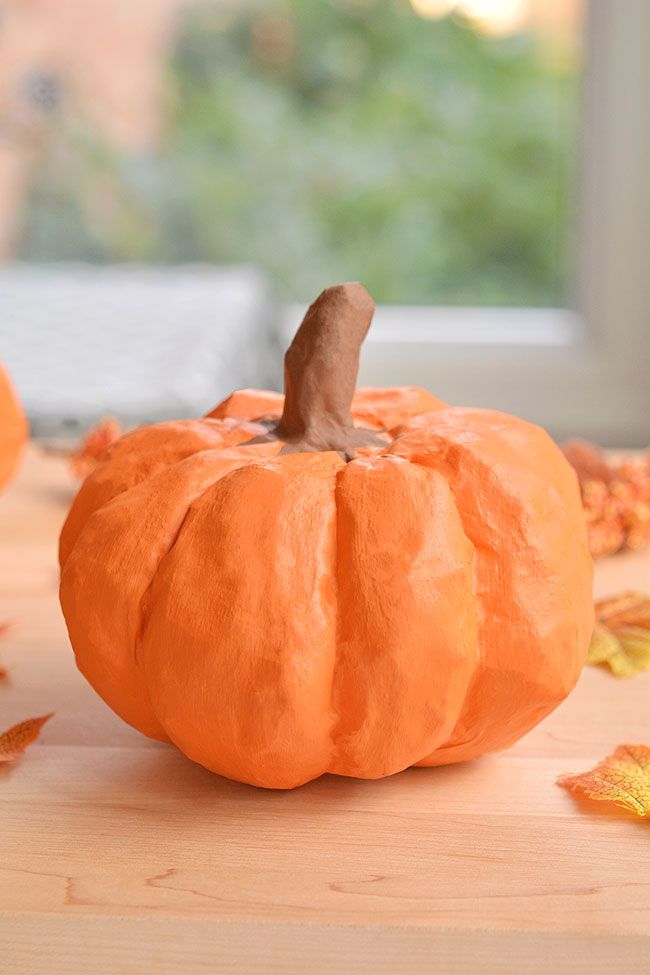 Artificial orange pumpkin on a wooden table, surrounded by autumn leaves, with a blurred background.