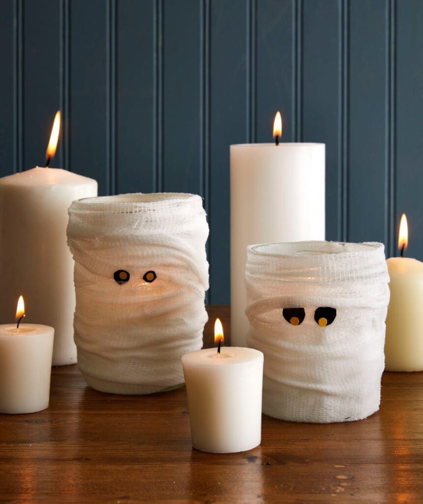 cbaa73c1d5cff33a02b81a3650531856 Halloween candle decor featuring mummy-wrapped jars with glowing eyes and white candles on a wooden table. | Sky Rye Design Halloween candle decor featuring mummy-wrapped jars with glowing eyes and white candles on a wooden table.