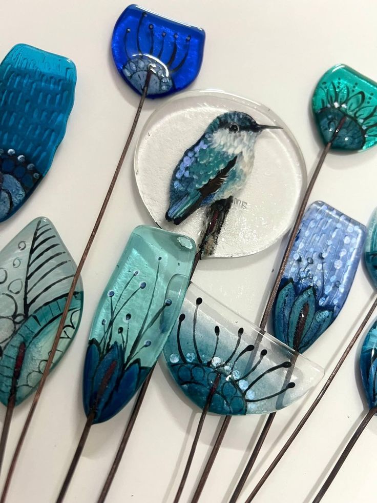 cca388b4-c5db-4529-b502-3db1db04d1f0 Blue and turquoise glass art featuring a bird and floral designs on thin stems. | Sky Rye Design Blue and turquoise glass art featuring a bird and floral designs on thin stems.