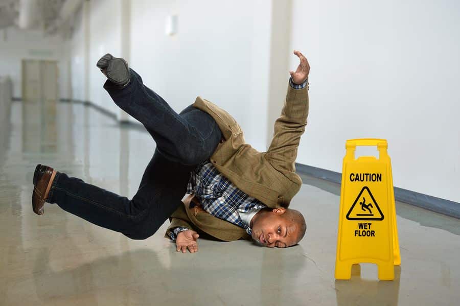 Man slips on wet floor near caution sign, highlighting workplace safety.