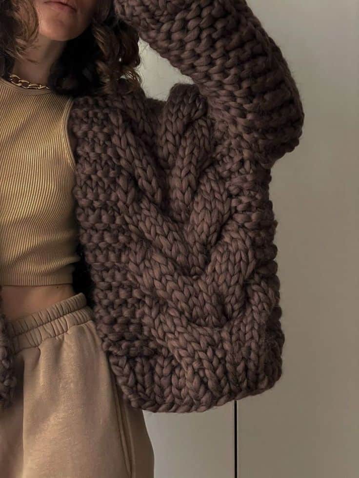 Woman wearing a chunky brown knit sweater and beige outfit in stylish, cozy fashion setting.