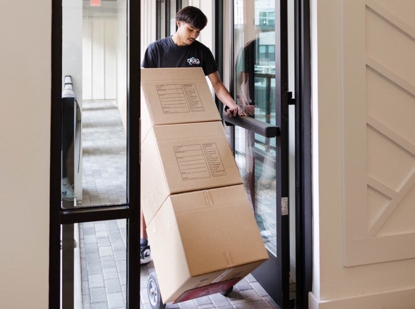 commercial Delivery person maneuvering a hand truck with boxes through a doorway indoors. | Sky Rye Design Delivery person maneuvering a hand truck with boxes through a doorway indoors.