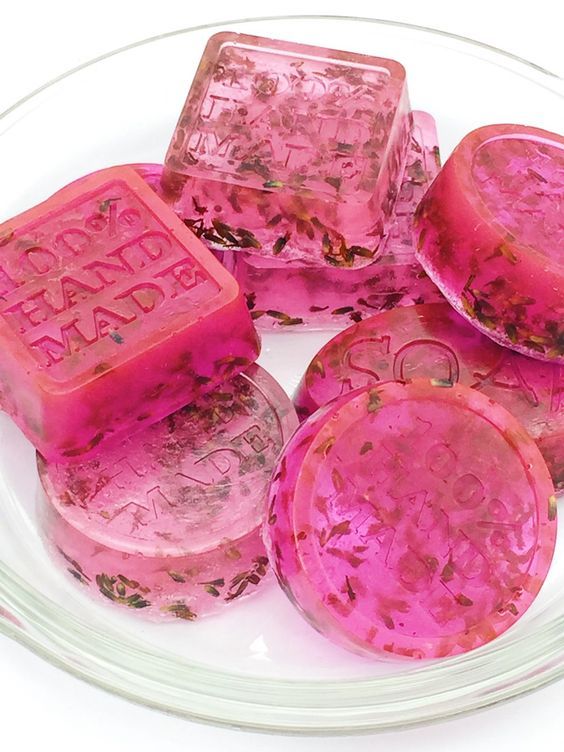 Handmade pink soap bars with floral inclusions in a glass dish.