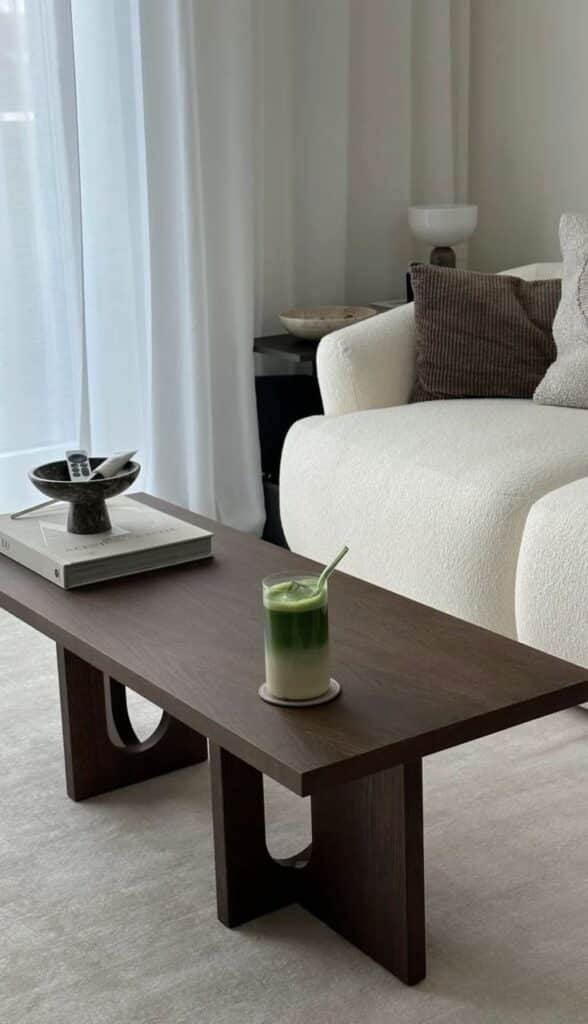 Cozy living room with a dark wood coffee table, matcha latte, and a plush white sofa with pillows.