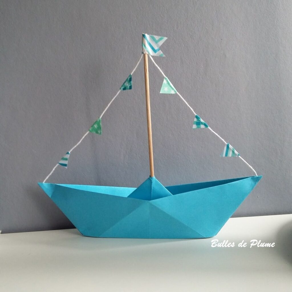 d1a4d2bfe9ee74b8f3b7453313c2ea2d Blue origami boat with small triangular flags, displayed against a gray background. | Sky Rye Design Blue origami boat with small triangular flags, displayed against a gray background.
