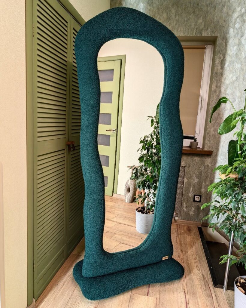 Unique curvy green-framed mirror in modern room with plants and wooden accents for stylish home decor.