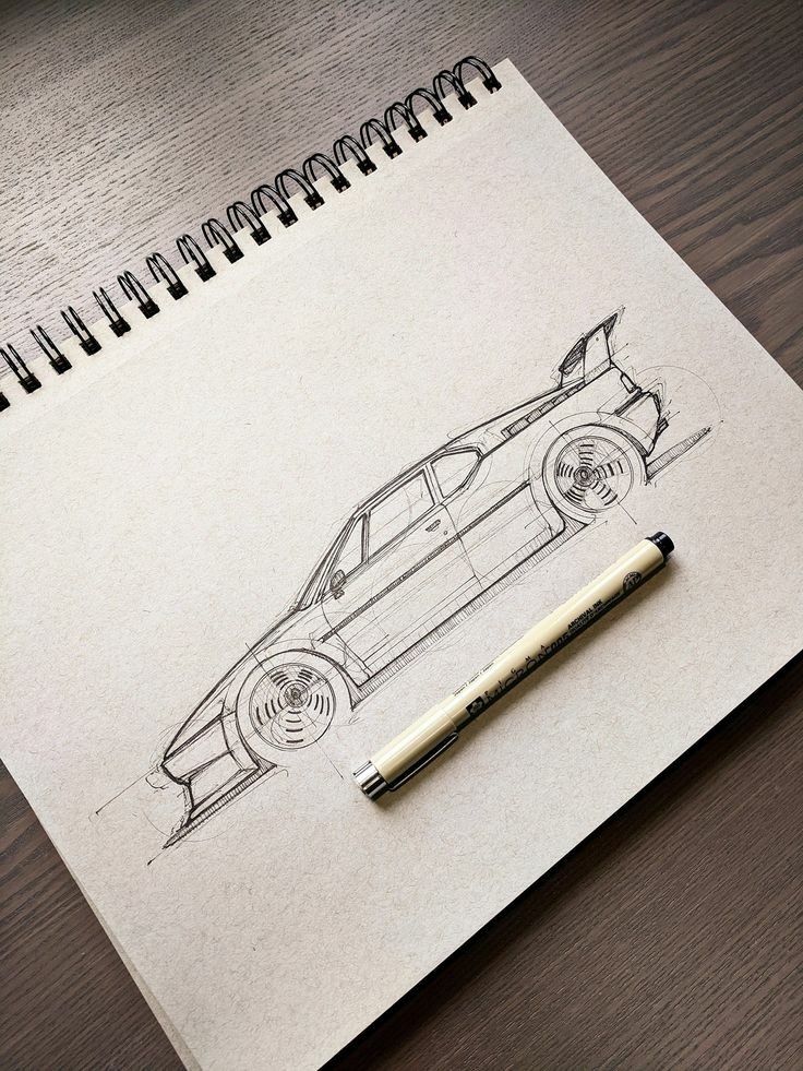 Sketch of a sports car with spoiler on a sketchpad, alongside a black pen, on a wooden table.