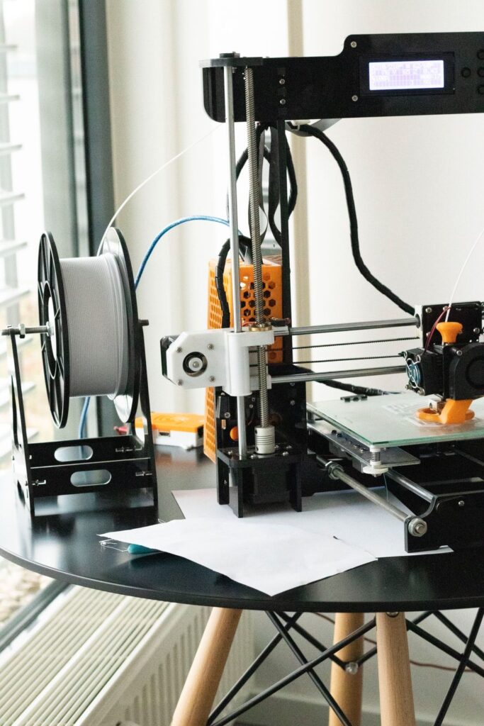3D printer with filament spool on table, near window, mid-print.