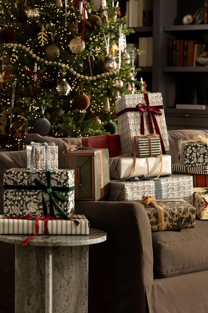 Holiday gifts wrapped in festive paper with bows, stacked by a decorated Christmas tree sparkling with lights.