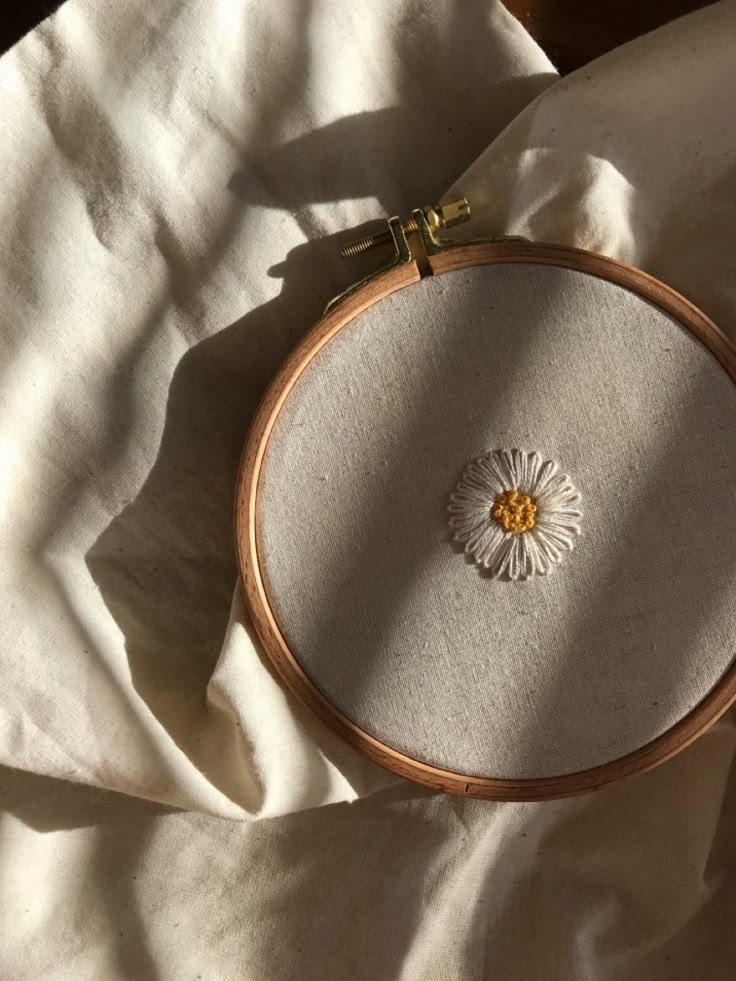 Embroidery hoop with a daisy design on cream fabric under sunlight.