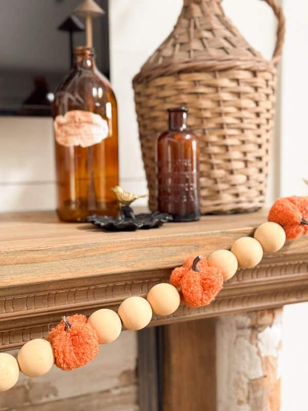 Rustic autumn decor: bottles and wicker vase on mantle with orange and beige garland.