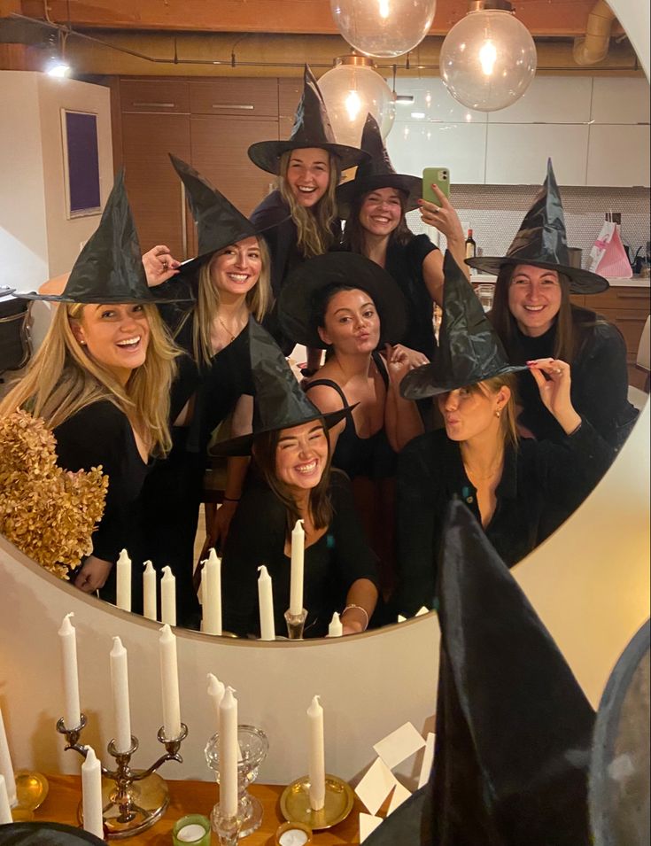 Group of friends dressed as witches posing in front of a mirror, with tall hats and candles on the table.