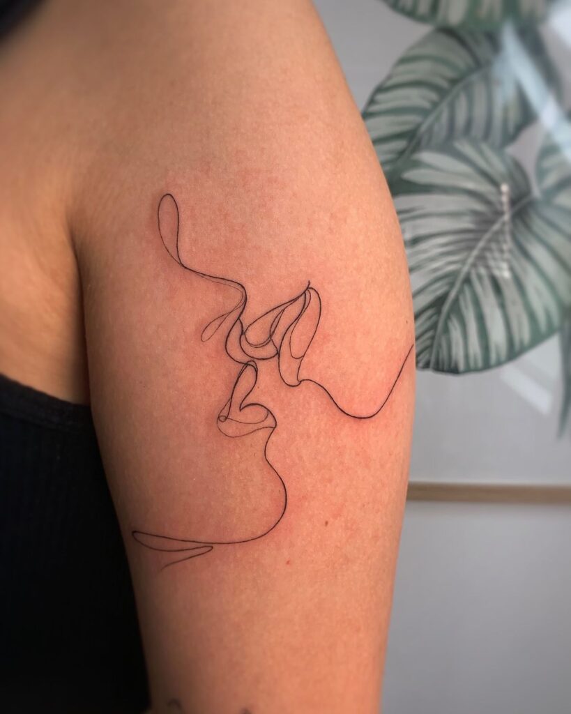 Minimalist line art tattoo on arm, depicting a single continuous line forming two faces intertwined.