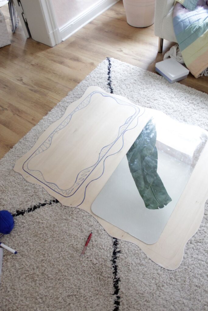 Decorative DIY mirror with artistic sketches on wooden board placed on a cozy rug in a living room.