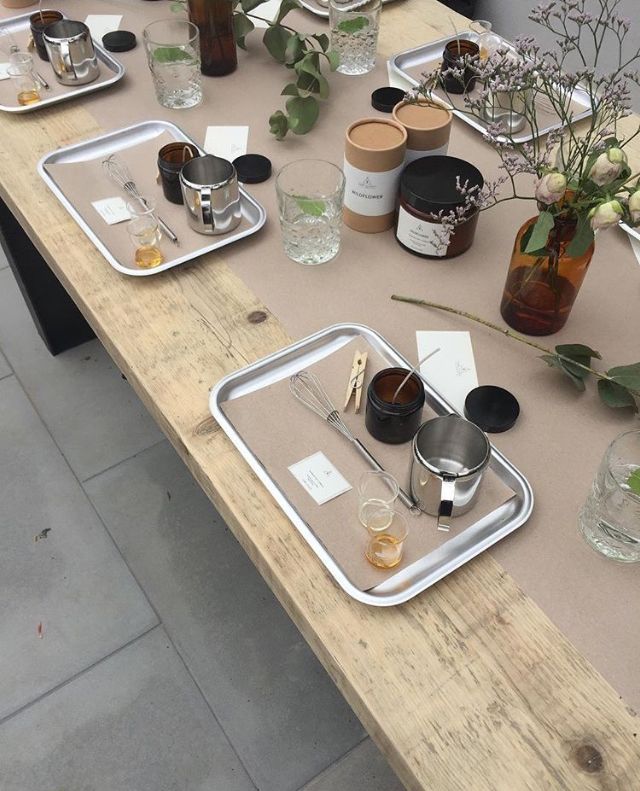 Candle-making workshop setup with trays, jars, and tools on a wooden table with decor.