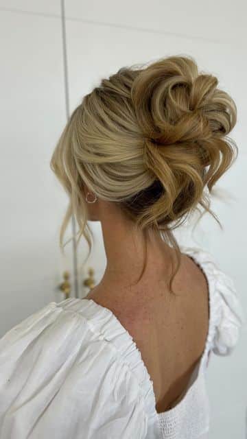Elegant updo hairstyle with soft curls and blonde highlights, perfect for weddings or formal events.