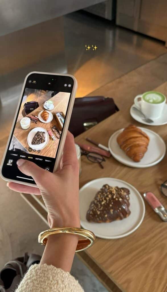 effdeesea✨ Person photographing a table with croissants, a matcha latte, and accessories using a smartphone in a cozy cafe setting. | Sky Rye Design Person photographing a table with croissants, a matcha latte, and accessories using a smartphone in a cozy cafe setting.