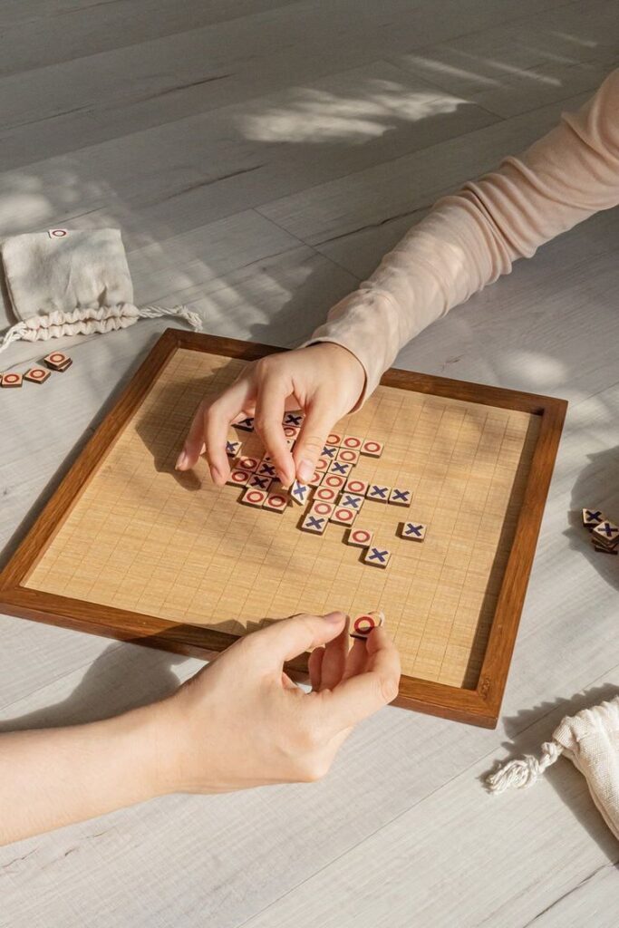 Hands playing a strategy board game with wooden pieces on a sunlit table.