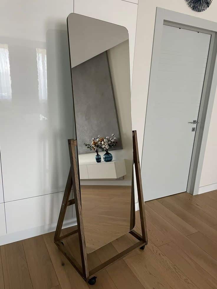 Modern full-length mirror with wooden frame on wheels in a stylish room with wooden floor and decor.