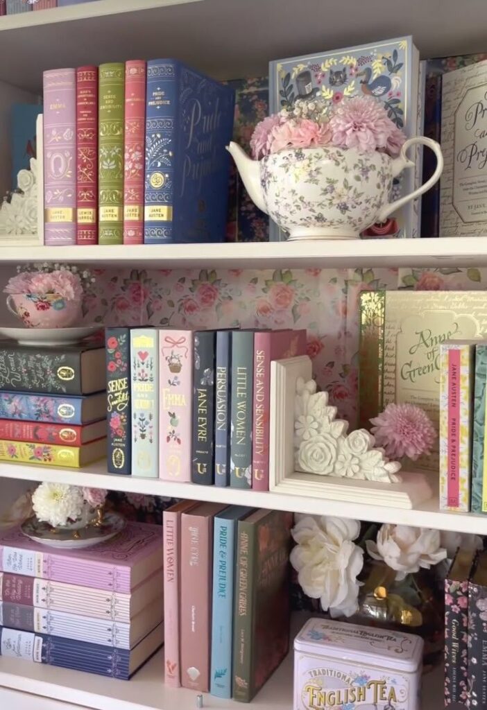 Colorful classic book collection on shelves with a floral teapot and decorative flowers. Cozy reading aesthetic.