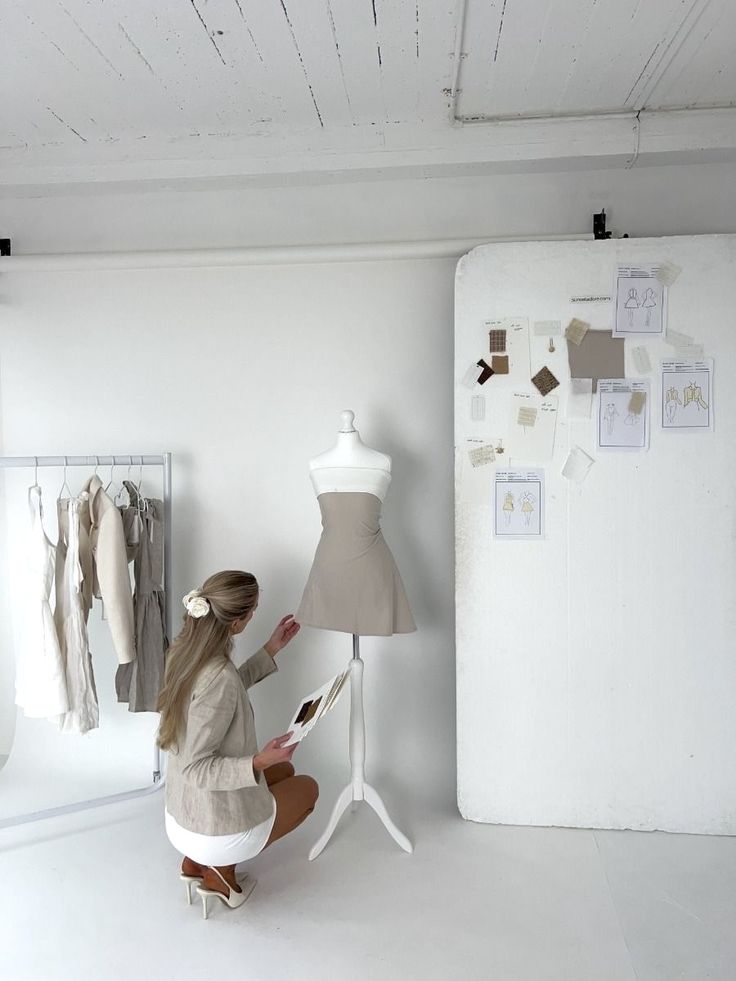 Fashion designer working on a beige dress mannequin in a studio with sketches and fabric samples.