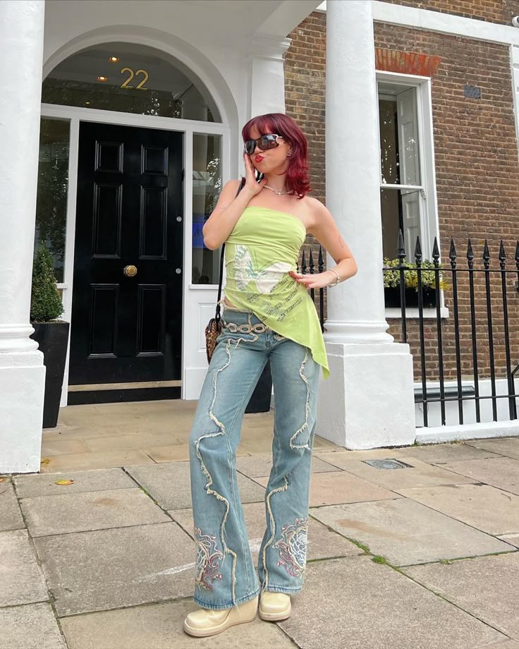 Fashionable person in green top and embroidered jeans poses outside a stylish townhouse.