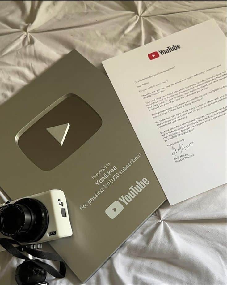 YouTube Silver Play Button Award and letter on a bed with a camera, celebrating 100,000 subscribers milestone.