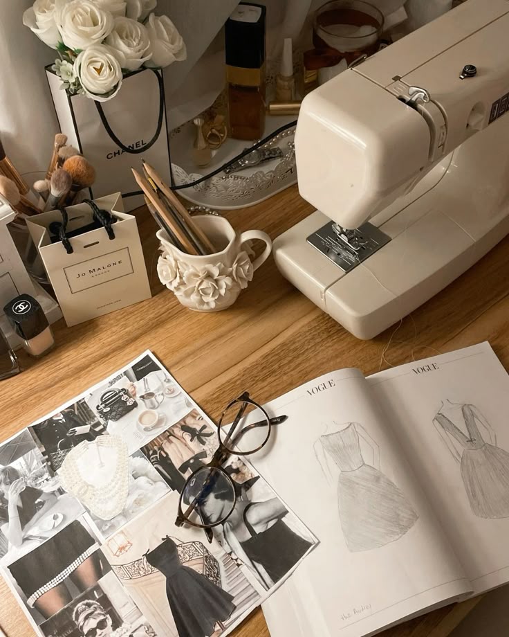 Vintage sewing setup with a sewing machine, fashion sketches, and elegant decor on a wooden table.