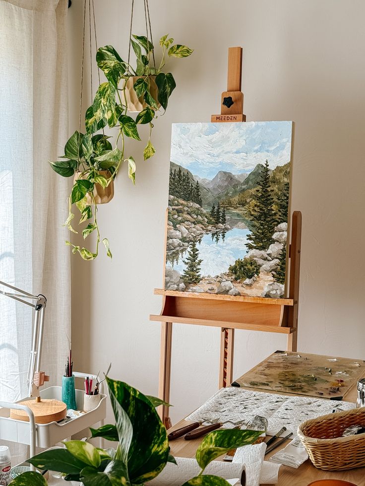 Painting of a serene mountain landscape on an easel, surrounded by indoor plants and art supplies in a cozy studio.