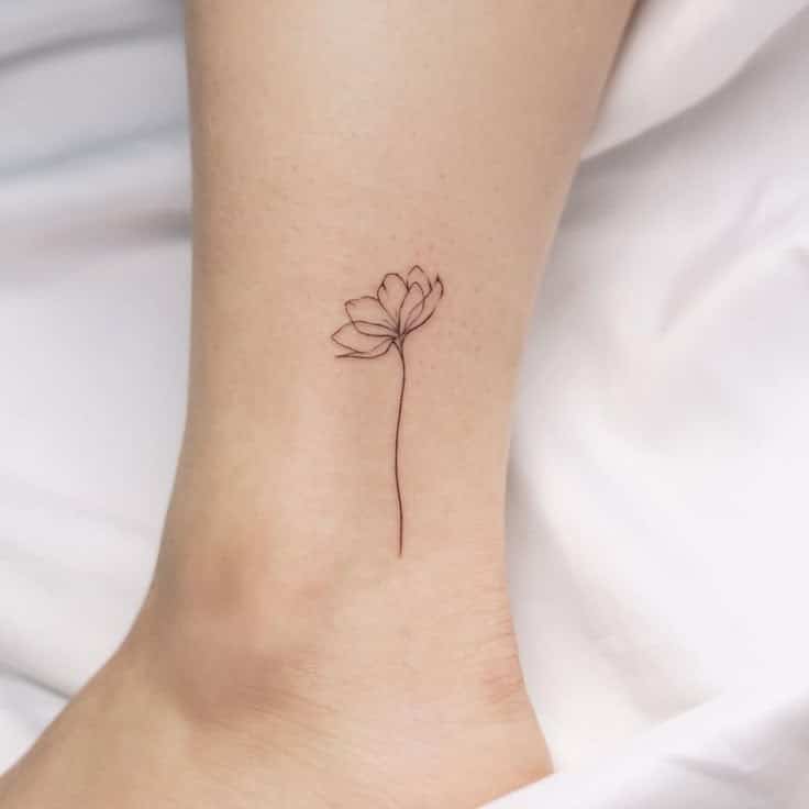 Minimalist flower tattoo on ankle, delicate line art on skin against white background.