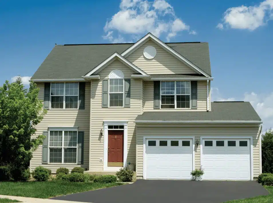 Two-story suburban house with a green lawn, blue sky, and attached garage.