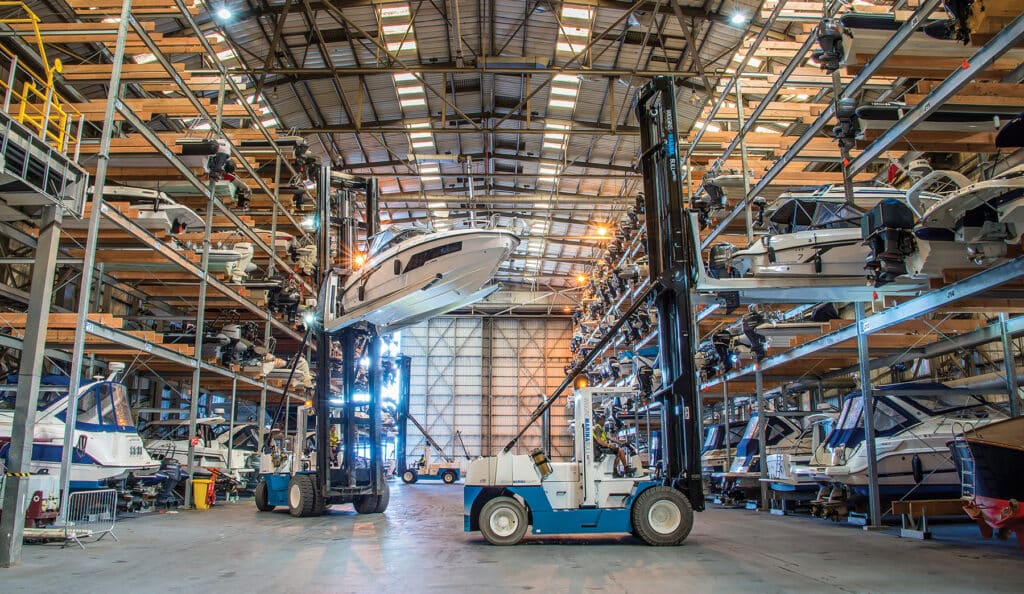 get-into-boating-boat-storage-dry-stack-hero Large indoor marina with stacked boat storage and a forklift placing a boat on a shelf. | Sky Rye Design Large indoor marina with stacked boat storage and a forklift placing a boat on a shelf.