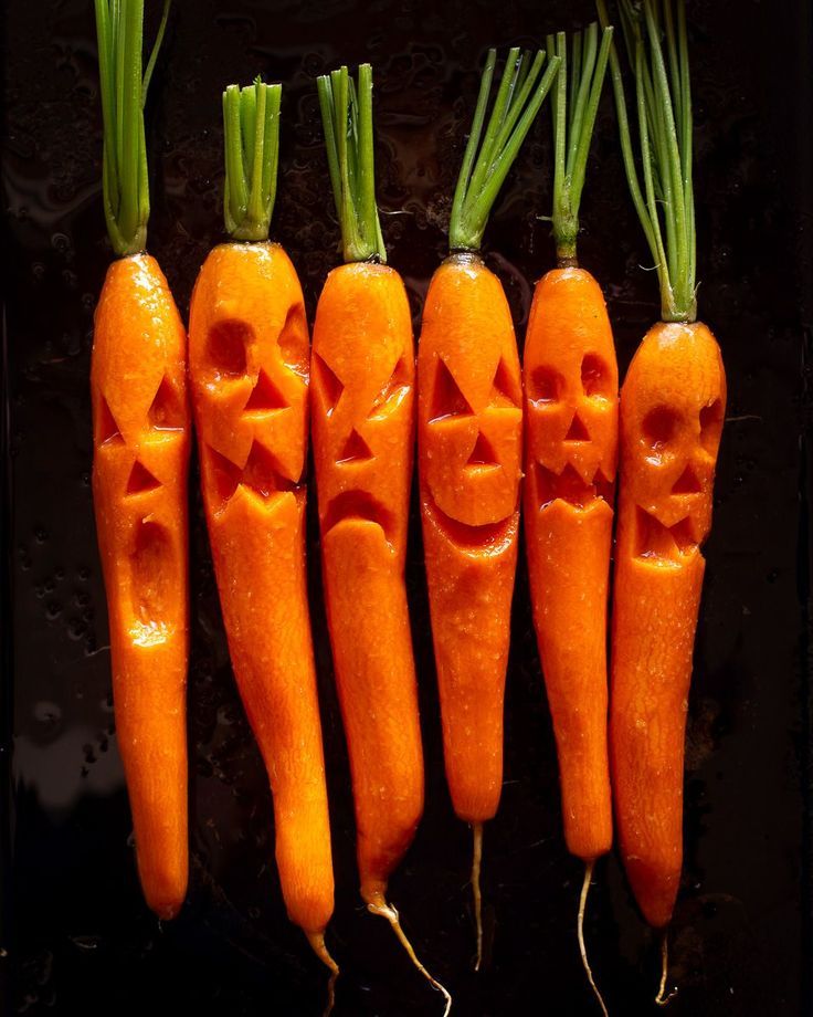 Carrots carved with spooky faces, resembling Halloween jack-o'-lanterns, displayed in a row.