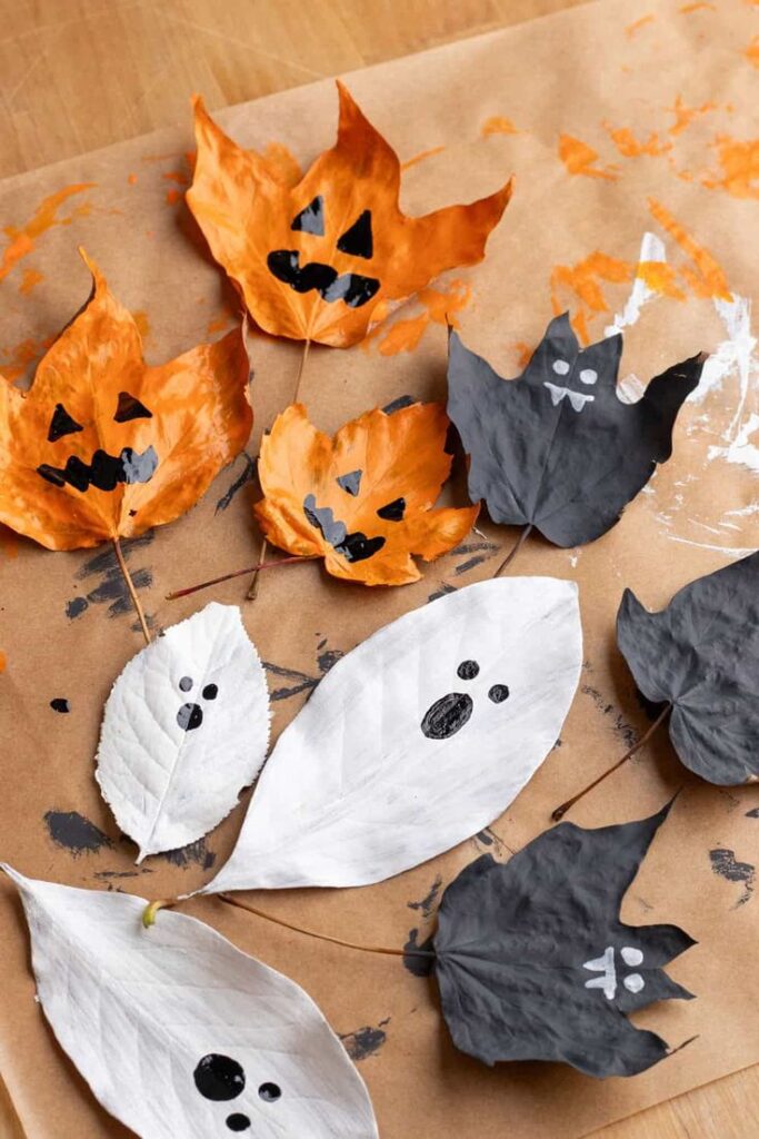 Halloween-themed leaves painted as ghosts and pumpkins on brown paper.