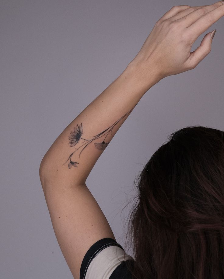 Forearm with floral tattoo, woman raising arm, neutral background.