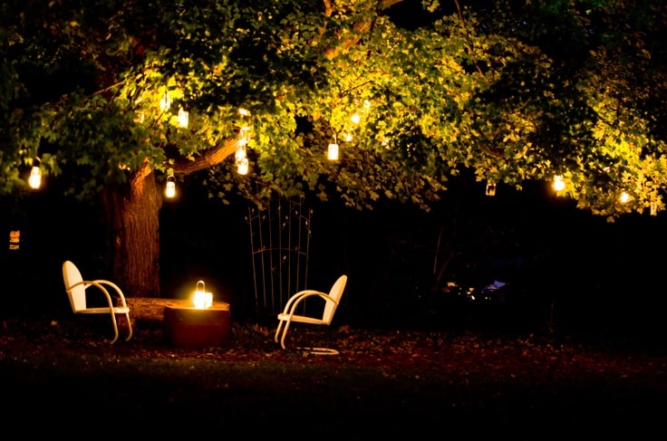 Cozy night scene with string lights and chairs under a tree, perfect for outdoor relaxation and ambiance.