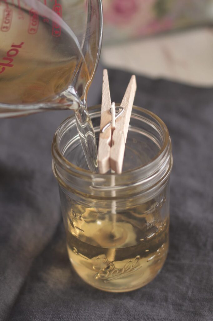 Pouring liquid into mason jar with clothespin, candle making process.