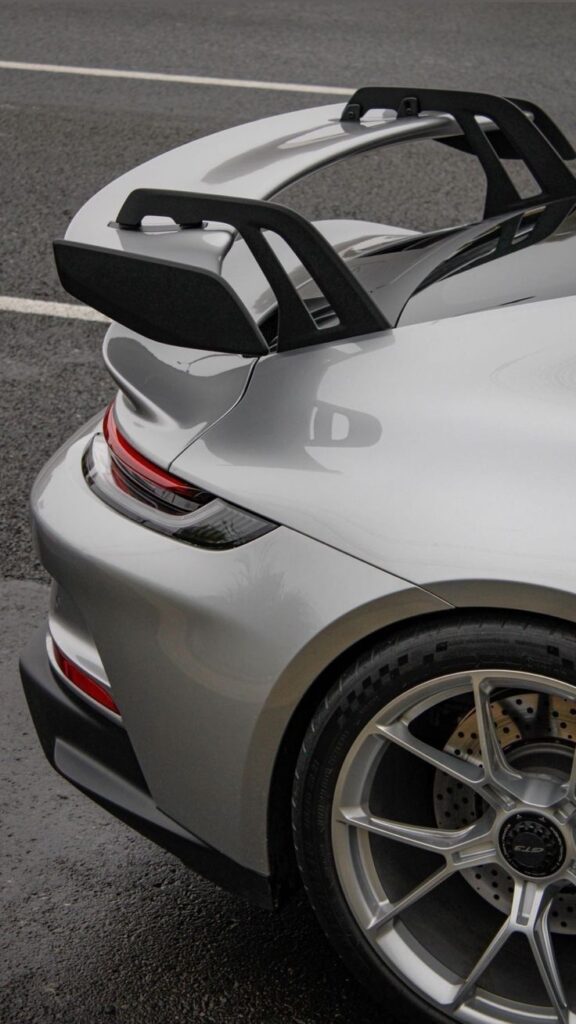 Silver sports car with sleek spoiler and alloy wheel, parked on wet asphalt.