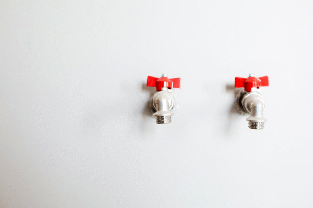 image Two metal faucets with red handles on a white wall, viewed from the front. | Sky Rye Design Two metal faucets with red handles on a white wall, viewed from the front.