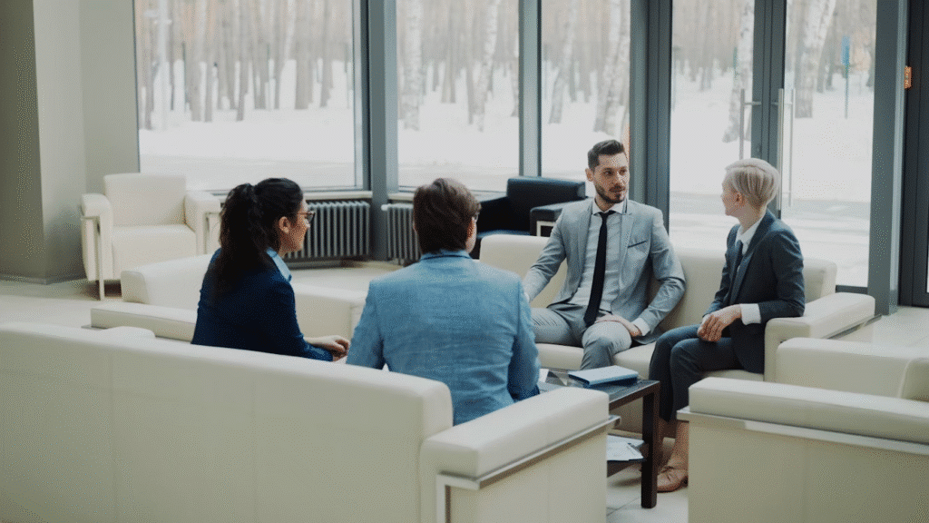 image Business meeting in a modern office with four professionals in suits discussing strategy on white sofas near large windows. | Sky Rye Design Business meeting in a modern office with four professionals in suits discussing strategy on white sofas near large windows.