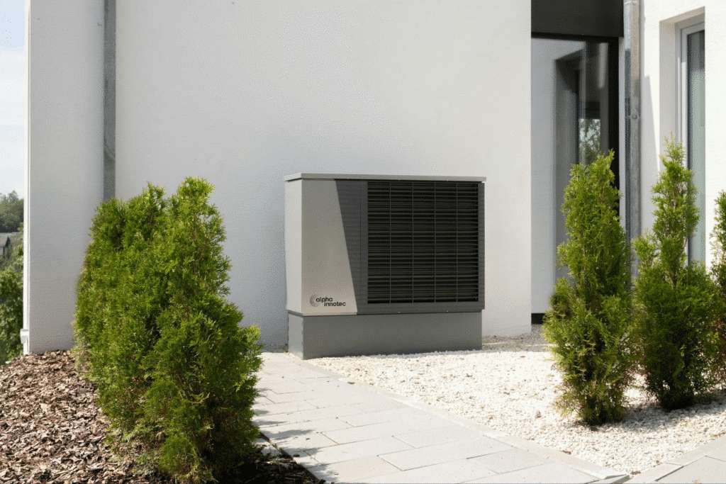 image Outdoor heat pump unit beside green shrubs on house exterior, efficient energy solution. | Sky Rye Design Outdoor heat pump unit beside green shrubs on house exterior, efficient energy solution.