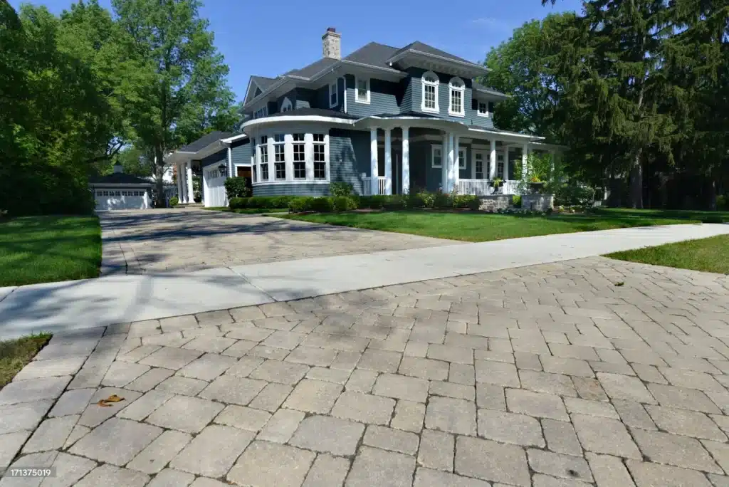 Elegant blue house with a spacious driveway and lush garden under a clear blue sky.